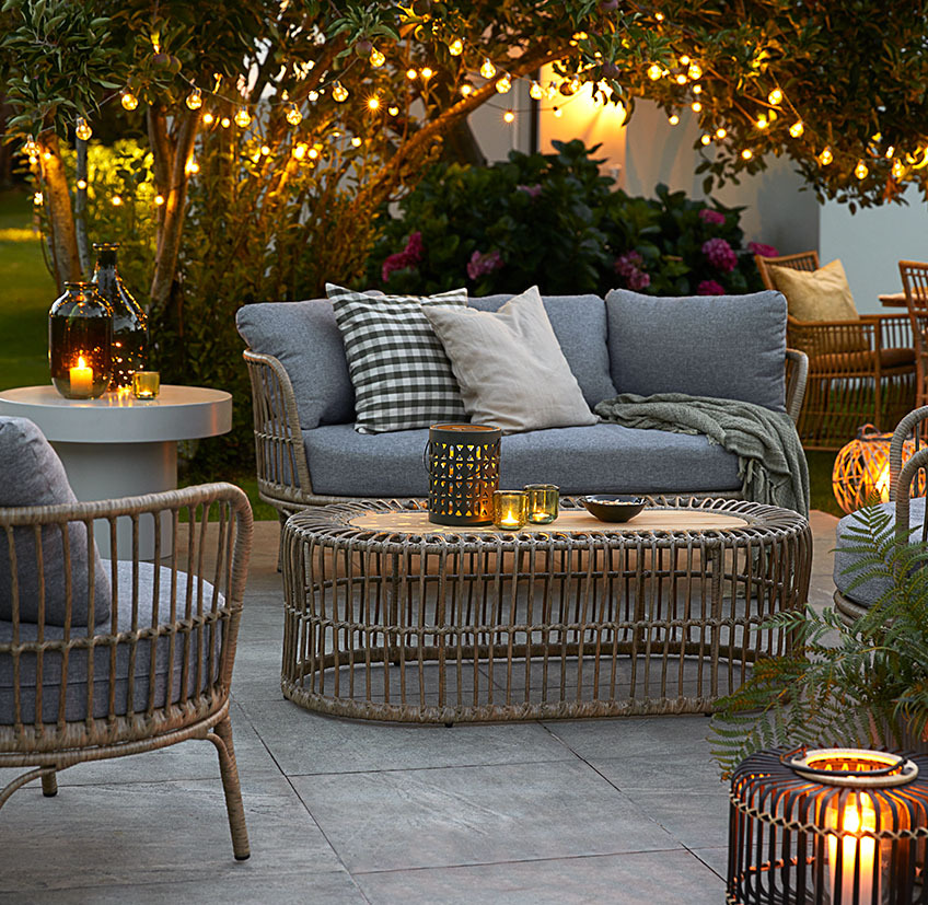 Una iluminación cálida es la mejor manera de crear el ambiente perfecto para una noche de verano. Cómodos muebles de salón en el patio con luces de cuerda, lámparas de pilas y farolillos con velas y candelitas